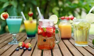 Mehrere bunte, fruchtige alkoholfreie Cocktails mit Beeren und Limette auf Holztisch.