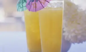 Zwei Gläser mit gelbem Saft und Eis, dekoriert mit kleinen bunten Schirmchen.