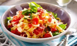 Nudeln mit Tomaten, Mozzarella, Basilikum und Speck in einer Schüssel.