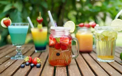 Mehrere bunte, fruchtige alkoholfreie Cocktails mit Beeren und Limette auf Holztisch.