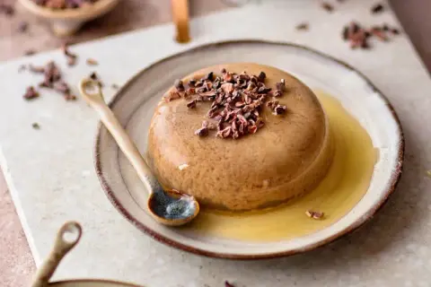 Schokoladenpudding mit Kakaonibs und Honig auf einem Teller mit Löffel.