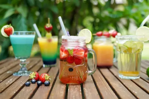 Mehrere bunte, fruchtige alkoholfreie Cocktails mit Beeren und Limette auf Holztisch.