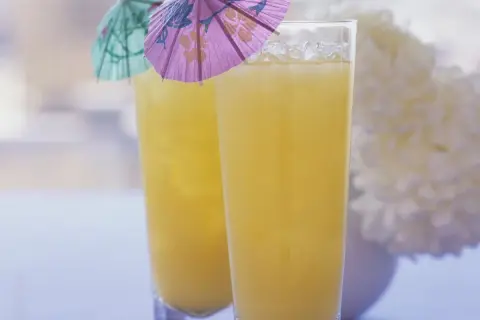 Zwei Gläser mit gelbem Saft und Eis, dekoriert mit kleinen bunten Schirmchen.