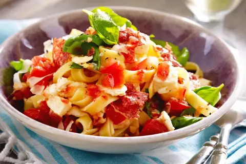 Nudeln mit Tomaten, Mozzarella, Basilikum und Speck in einer Schüssel.