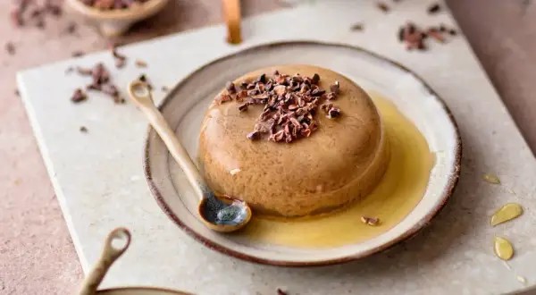 Schokoladenpudding mit Kakaonibs und Honig auf einem Teller mit Löffel.