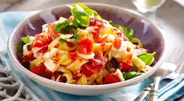 Nudeln mit Tomaten, Mozzarella, Basilikum und Speck in einer Schüssel.