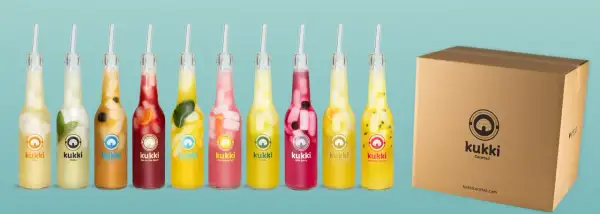 Reihe von Kukki Cocktails in Flaschen mit Früchten und Eis, daneben eine Pappbox.