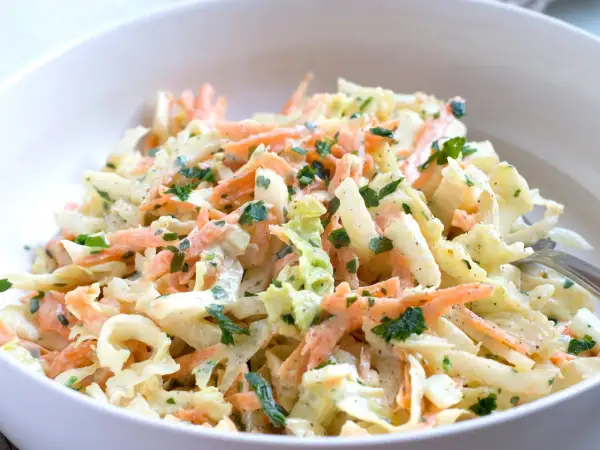 Chinakohl-Salat mit Karottenstreifen und Petersilie in einer weißen Schüssel.