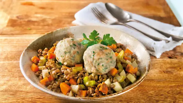 Zwei Semmelknödel auf Linsengemüse mit Karotten und Sellerie, garniert mit Petersilie.