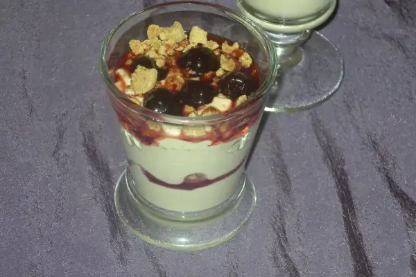 Dessert im Glas mit Kirschen, zerbröseltem Keks und Fruchtsauce.