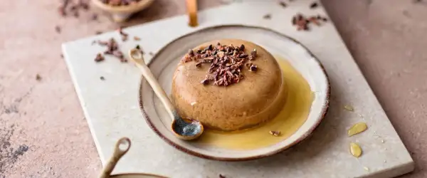 Schokoladenpudding mit Kakaonibs und Honig auf einem Teller mit Löffel.