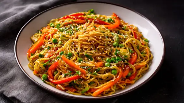 Schüssel mit chinesischen Bratnudeln, garniert mit Erbsen, Paprika und Sesam.