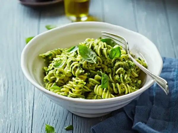Eine Schüssel Fusilli-Nudeln mit grünem Pesto und frischem Basilikum, garniert mit einer Gabel.