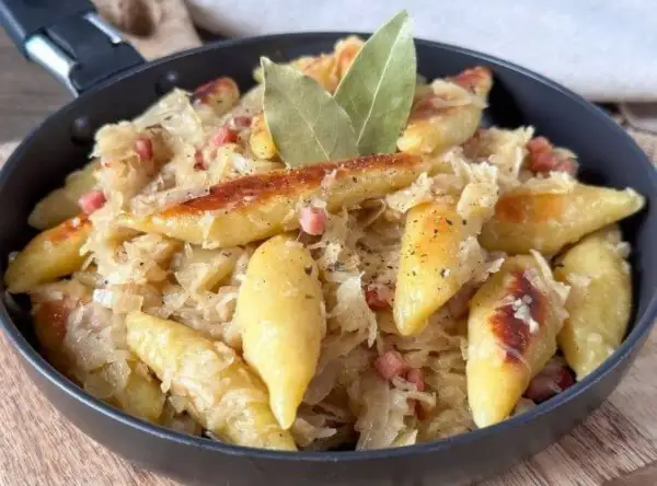 Nudeln mit Sauerkraut und Speck in einer Pfanne, garniert mit Lorbeerblättern.