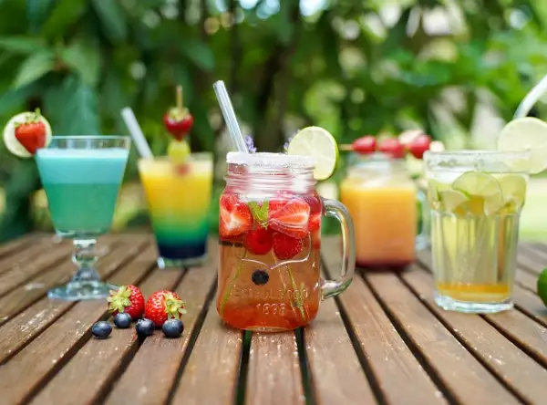 Mehrere bunte, fruchtige alkoholfreie Cocktails mit Beeren und Limette auf Holztisch.