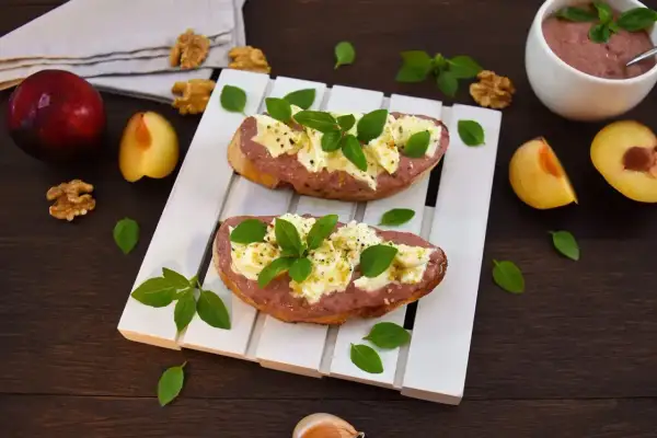 Zwei Bruschettas mit Pflaumenaufstrich, Käse und Basilikum, garniert mit Walnüssen und frischen Pflaumen.