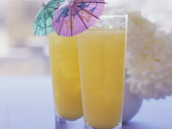 Zwei Gläser mit gelbem Saft und Eis, dekoriert mit kleinen bunten Schirmchen.