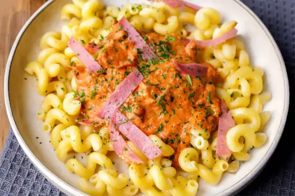 Gedrehte Nudeln mit cremiger Tomatensoße und rosa Wurststreifen, garniert mit Petersilie.
