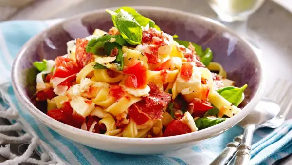 Nudeln mit Tomaten, Mozzarella, Basilikum und Speck in einer Schüssel.