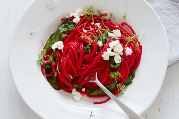 Rote-Bete-Spaghetti mit Spinat, Feta und Kresse auf einem Teller.