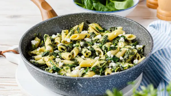 Penne-Nudeln mit Spinat und zerbröseltem Feta in einer Pfanne.