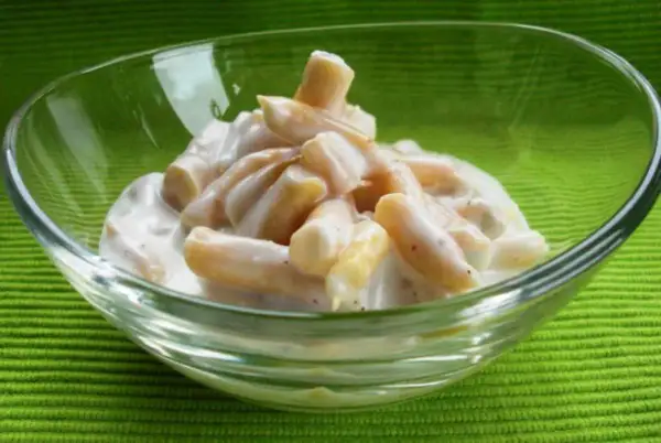 Gelber Bohnensalat in einer Glasschüssel auf grünem Hintergrund.